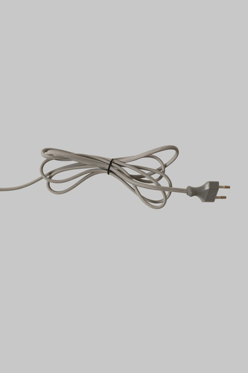 Netzkabel mit Eurostecker in Sand, zu einer lockeren Schlaufe gebunden, auf neutralem grauem Hintergrund.