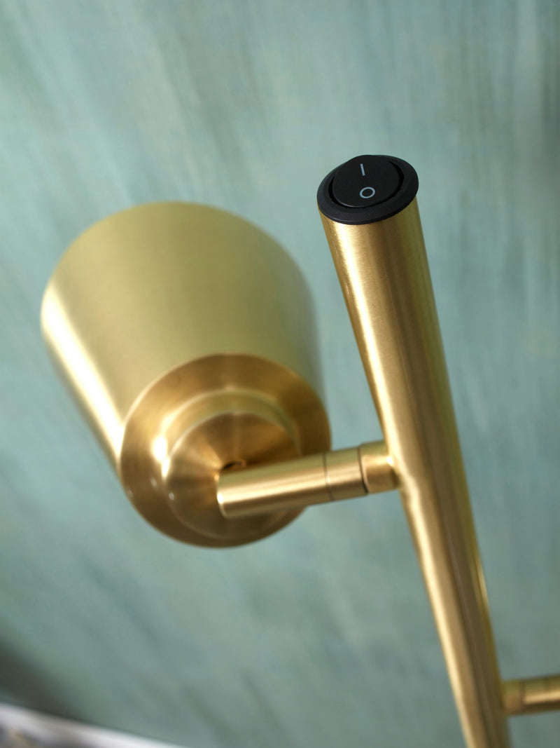 Detailansicht einer goldfarbenen Stehleuchte mit gebürsteter Metallschirmhalterung, schwenkbarem Gelenk und schwarzem Schalter am Stab.