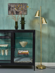 Stehleuchte It's about RoMi Bremen in Gold mit zwei schwenkbaren Schirmen neben einer schwarzen Glasvitrine.