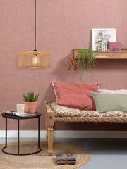 Hängeleuchte Bromo aus Bambus in Natur/Schwarz über einem Sofa mit rosa und grünen Kissen vor rosa Wand