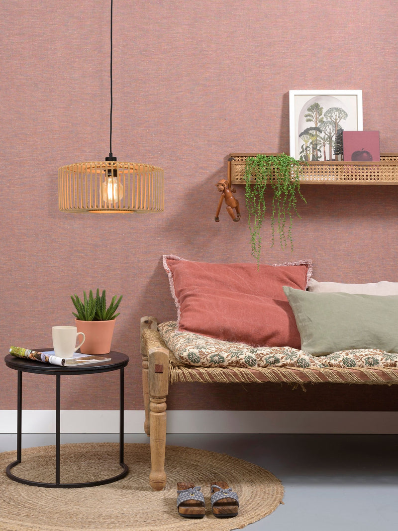Hängeleuchte Bromo aus Bambus in Natur/Schwarz über einem Sofa mit rosa und grünen Kissen vor rosa Wand
