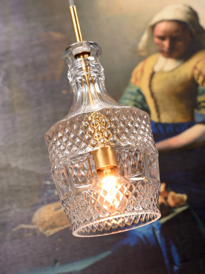 RoMi Hängeleuchte Brussels mit goldenem Fassungsteil und transparentem Glas, eingeschaltet vor einem Gemälde.