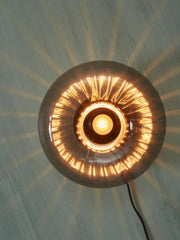 Runde Glas-Wandleuchte RoMi Brussels von vorn, mit leuchtender Glühlampe und Lichtschein an der Wand.