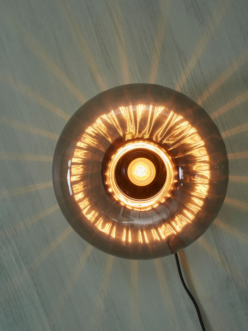 Runde Glas-Wandleuchte RoMi Brussels von vorn, mit leuchtender Glühlampe und Lichtschein an der Wand.