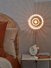 Runde Wandleuchte Brussels von RoMi mit leuchtendem Glasring und goldfarbener Fassung in einem Schlafzimmer.