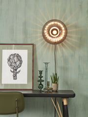 Wandleuchte It's about RoMi Brussels mit rundem, rauchgrauem Glasschirm und leuchtendem Lichtspiel an einer grünen Wand.
