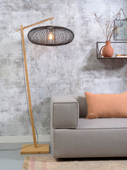 Stehleuchte Cango von Good&Mojo mit Bambusgestell und dunklem Geflechtschirm, neben einem grauen Sofa aufgestellt.