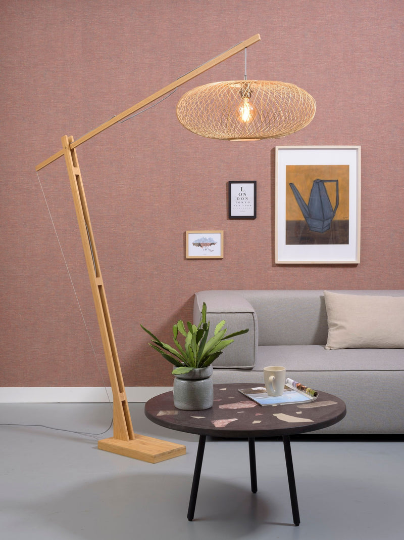 Gesamtansicht der Good&Mojo Stehleuchte Cango mit Bambusgestell und geflochtenem Schirm in Naturfarbe, daneben ein graues Sofa.