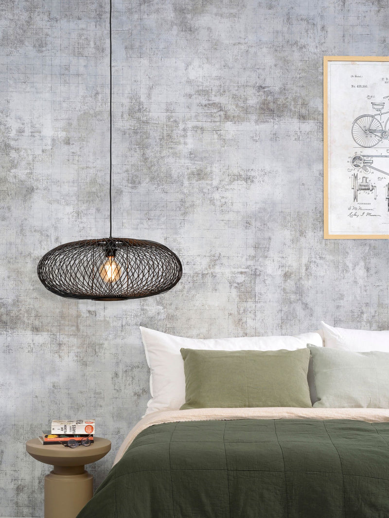Schwarze Hängeleuchte Cango von Good&Mojo mit ovalem Bambusgeflecht über einem Bett in einem Schlafzimmer mit Betonoptik.