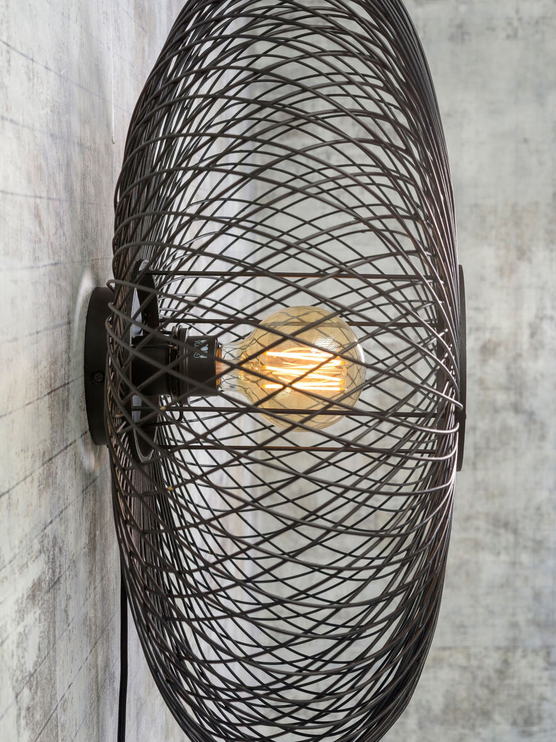Wandleuchte Cango von Good&Mojo mit schwarzem Drahtgeflecht-Schirm und sichtbarer Glühlampe vor grauer Betonwand.
