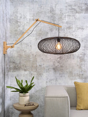 Wandleuchte Cango von Good&Mojo mit Bambusarm und schwarzem Gittergeflecht-Schirm, vor Betonoptik-Wand im Wohnraum.