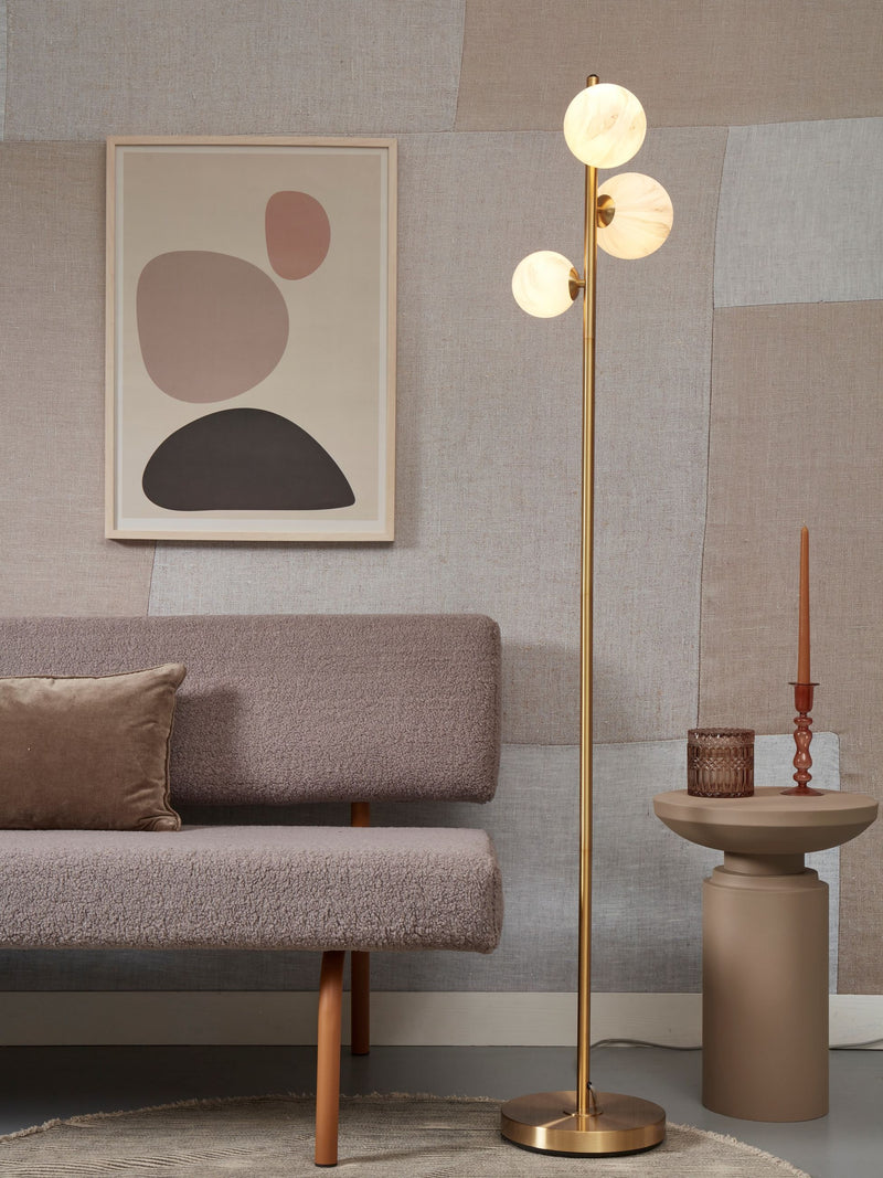 Stehleuchte It's about RoMi Carrara in Gold mit drei weißen Marmorglas-Kugelschirmen, im Wohnzimmer neben einem Sofa.