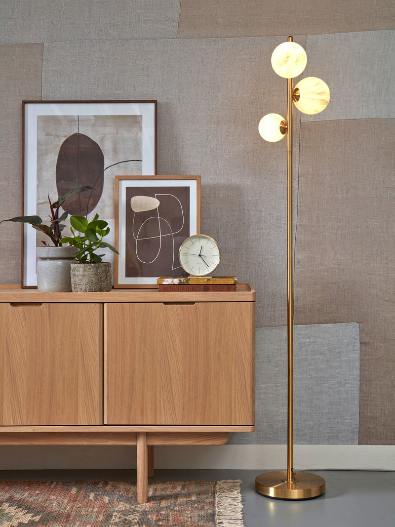 It’s about RoMi Stehleuchte Carrara Eisen Gold/Rauchglas mit drei Glaskugeln an goldenem Stab, neben einem Sideboard