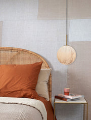 Hängeleuchte "It's about RoMi Carrara" mit marmoriertem Glasschirm in Weiß und Gold, über einem Bett mit Rattan-Kopfteil.