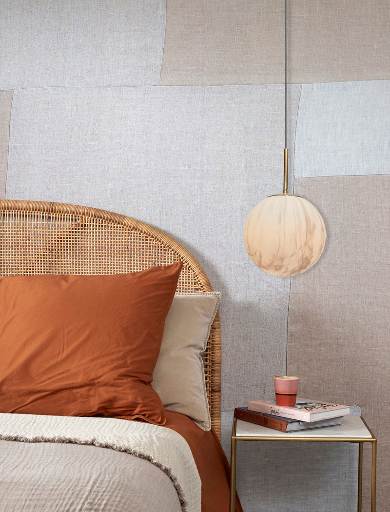 Hängeleuchte "It's about RoMi Carrara" mit marmoriertem Glasschirm in Weiß und Gold, über einem Bett mit Rattan-Kopfteil.
