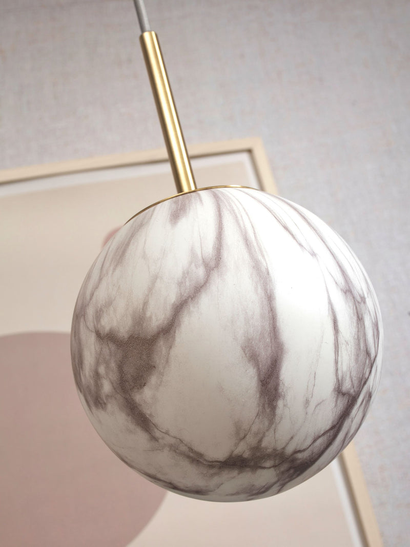 RoMi Hängeleuchte Carrara: Kugelförmiger Glasschirm in Marmoroptik mit grau-weißen Adern, goldene Stange.