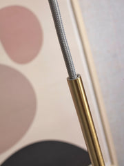 Detailansicht des goldfarbenen Metallstabs mit grauem Textilkabel vor einem beige-rosa Hintergrund mit Motiv