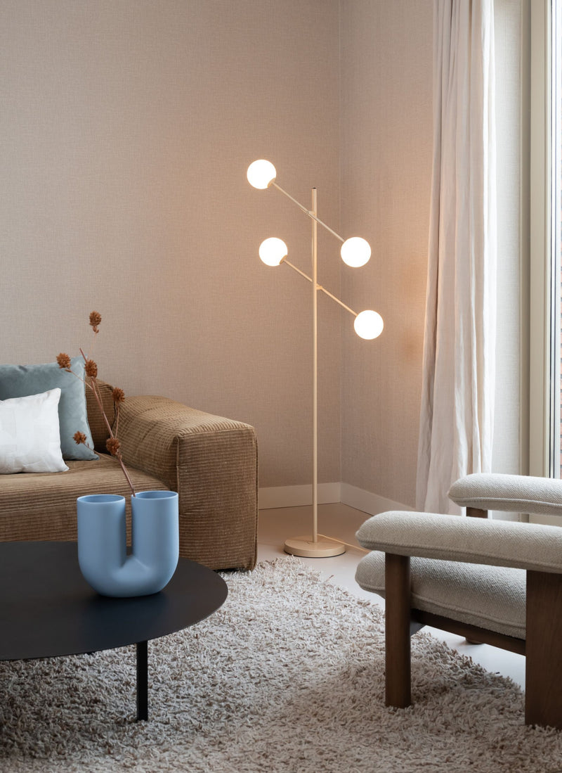 Stehleuchte It's about RoMi Copenhagen in Beige mit vier weißen Glaskugeln am Eisengestell, neben einem Sofa im Wohnraum.