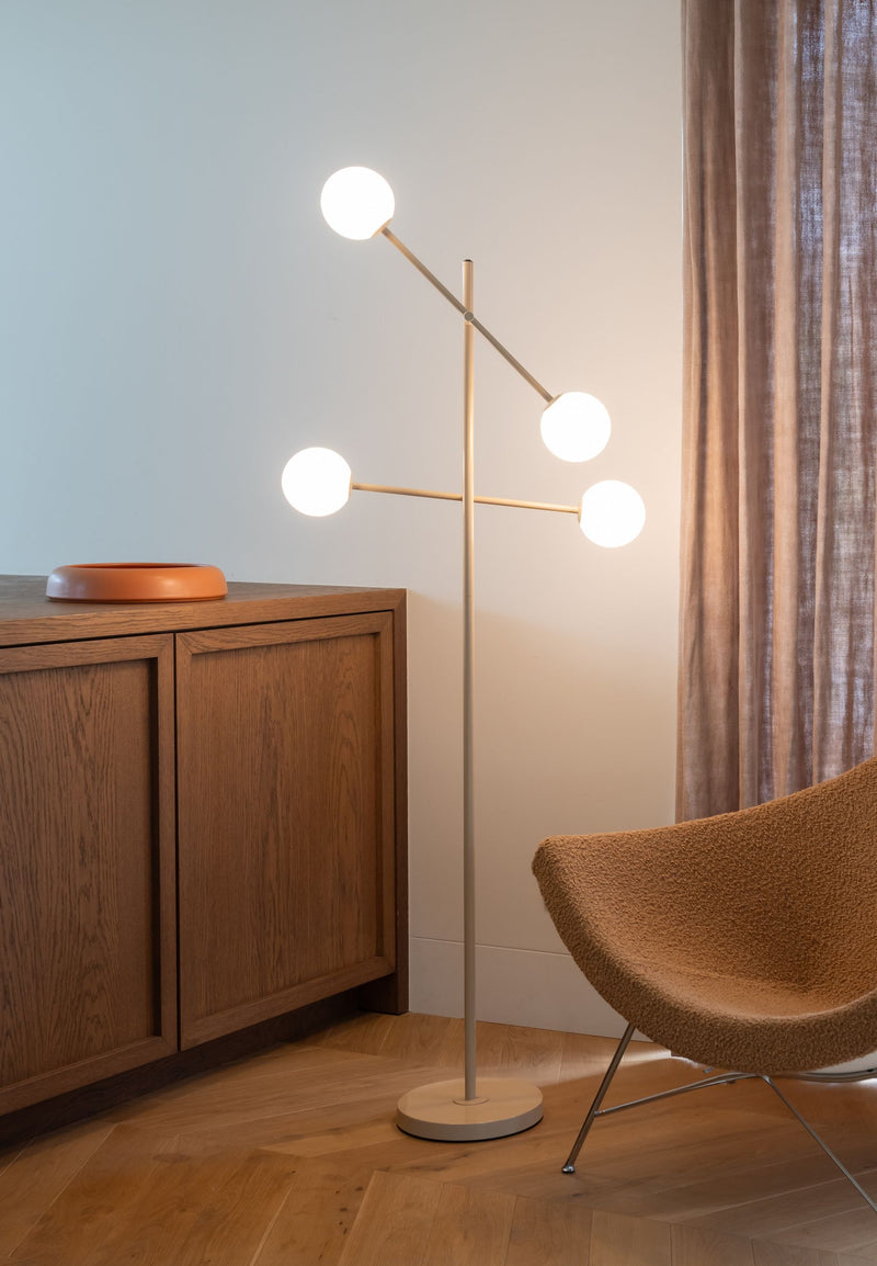 Stehleuchte "It's about RoMi Copenhagen" in Beige mit vier weißen Glaskugeln an einem schlanken Eisengestell, neben einem Holzsideboard.