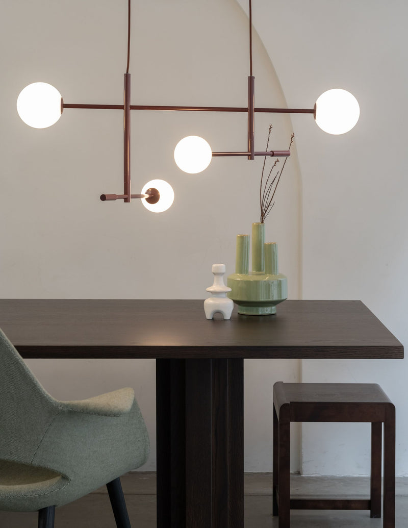 Pendelleuchte RoMi Copenhagen mit vier weißen Glaskugeln an bordeauxfarbenen Eisenstäben über einem Holztisch.