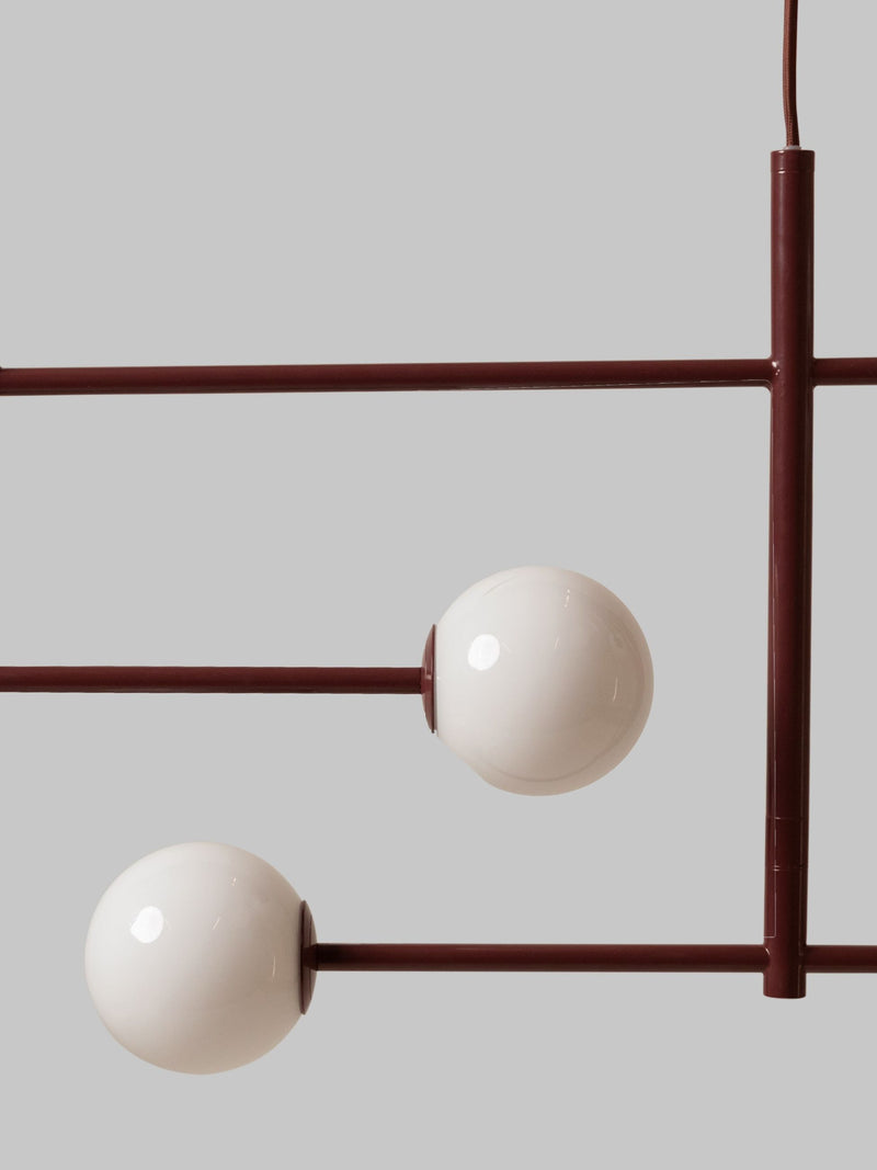 Detailansicht der Pendelleuchte It's about RoMi Copenhagen mit bordeauxrotem Eisengestell und zwei weißen Glaskugeln.