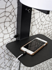 RoMi Wandleuchte Florence: Detailansicht der schwarzen Metallablage mit Smartphone und USB-Kabel, vor gemustertem Hintergrund.
