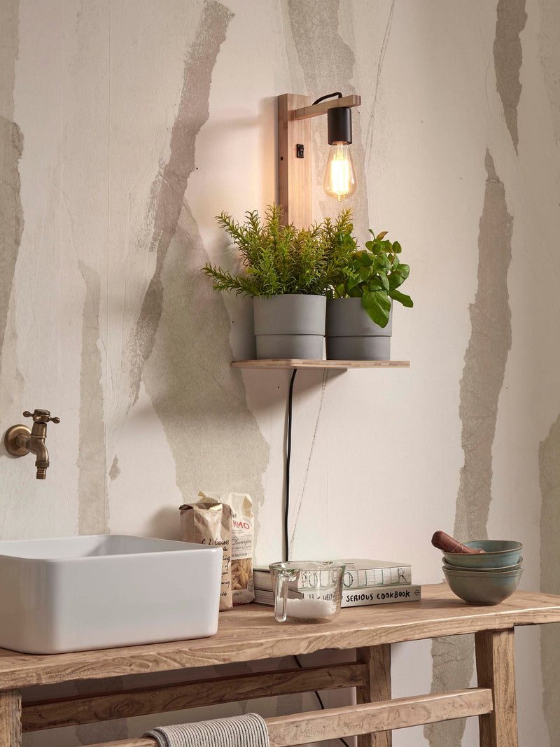 Wandleuchte Flores aus Bambus in Natur mit Ablage, daneben Kräutertöpfe und Glühbirne sichtbar an heller Wand.