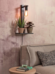 Good&Mojo Wandleuchte Flores aus schwarzem Bambus mit Ablage, an der Wand eingeschaltet, mit zwei Pflanzen und Glühbirne.