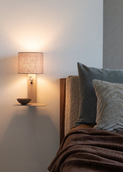 It's about RoMi Wandleuchte Florence mit rundem Leinenschirm und Ablage, über einem Bett mit Kissen und Decke fotografiert.