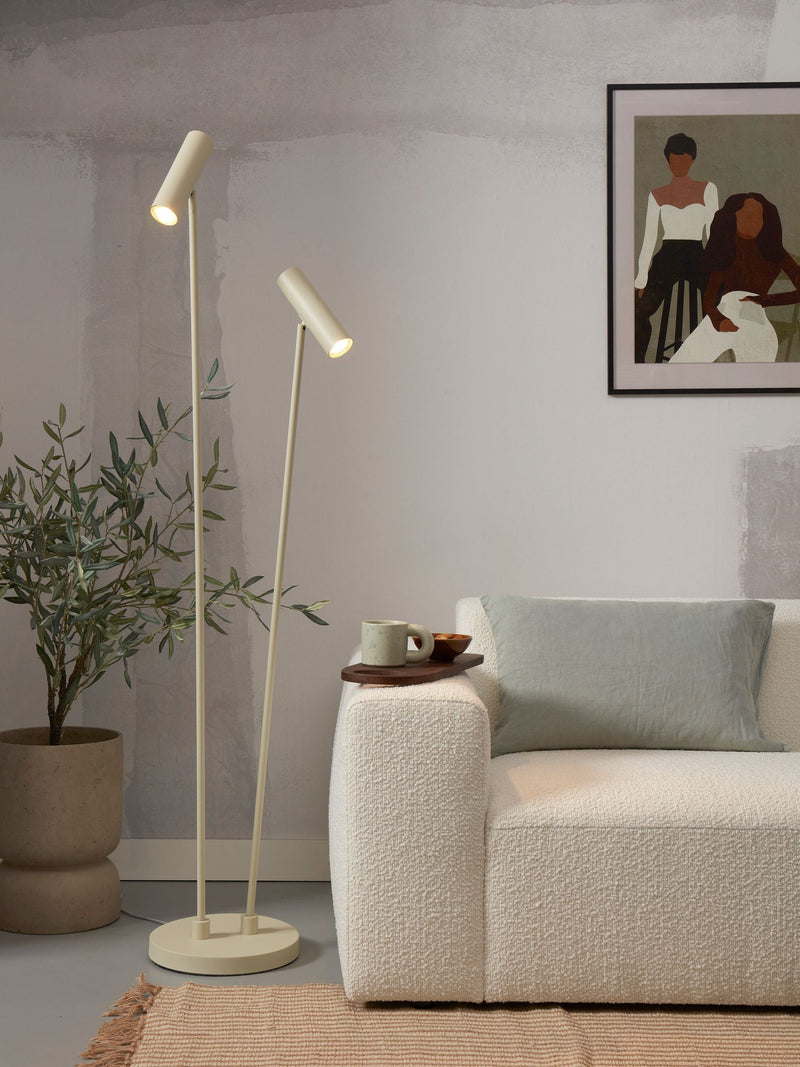 Stehleuchte mit zwei Leuchtköpfen in Beige/Creme vor einem Sofa mit Bouclé-Bezug.