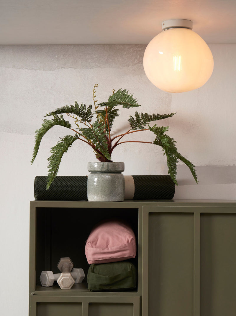 Die Deckenleuchte Helsinki mit weißem Kugelschirm aus Glas leuchtet über einem olivgrünen Schrank.