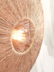 Detailansicht der Wandleuchte Good&Mojo Iguazu mit rund geflochtenem Jute-Schirm in Natur, durch die Öffnung leuchtet die Glühbirne.