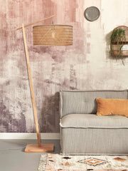 Good&Mojo Stehleuchte Java aus Bambus mit geflochtenem Naturschirm, im Wohnraum vor rosa-beiger Wand neben einem grauen Sofa.