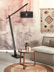 Stehleuchte Java XL von Good&Mojo mit schwarzem Bambusgestell und geflochtenem Schirm, schräg über einem Sofa im Wohnraum.