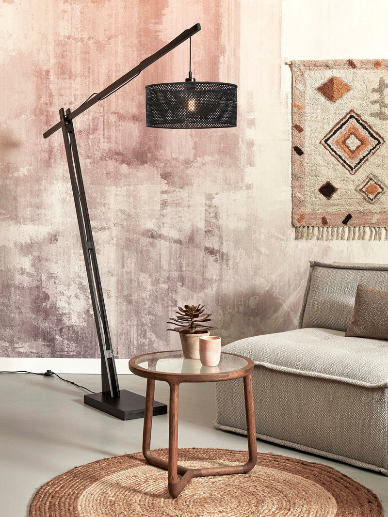 Stehleuchte Java XL von Good&Mojo mit schwarzem Bambusgestell und geflochtenem Schirm, schräg über einem Sofa im Wohnraum.
