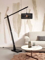 Stehleuchte Java XL von Good&Mojo mit schwarzem Bambusgestell und rundem Geflechtschirm, vor einer Sofa-Ansicht.