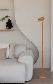 Stehleuchte Java von Good&Mojo mit schlankem Bambusstab und Bambusschirm vor beiger Wand neben einem hellen Sofa.