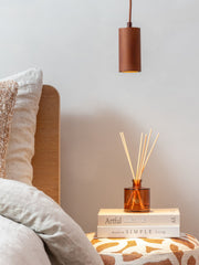 Good&Mojo Hängeleuchte Java aus Bambus in Braun hängt über einem Bett mit Holzkopfteil, daneben ein Diffuser auf Büchern.