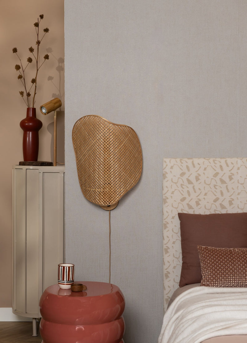Wandleuchte aus geflochtenem Rattan mit Stoffkabel über einem Bett an hellgrauer Wand montiert.