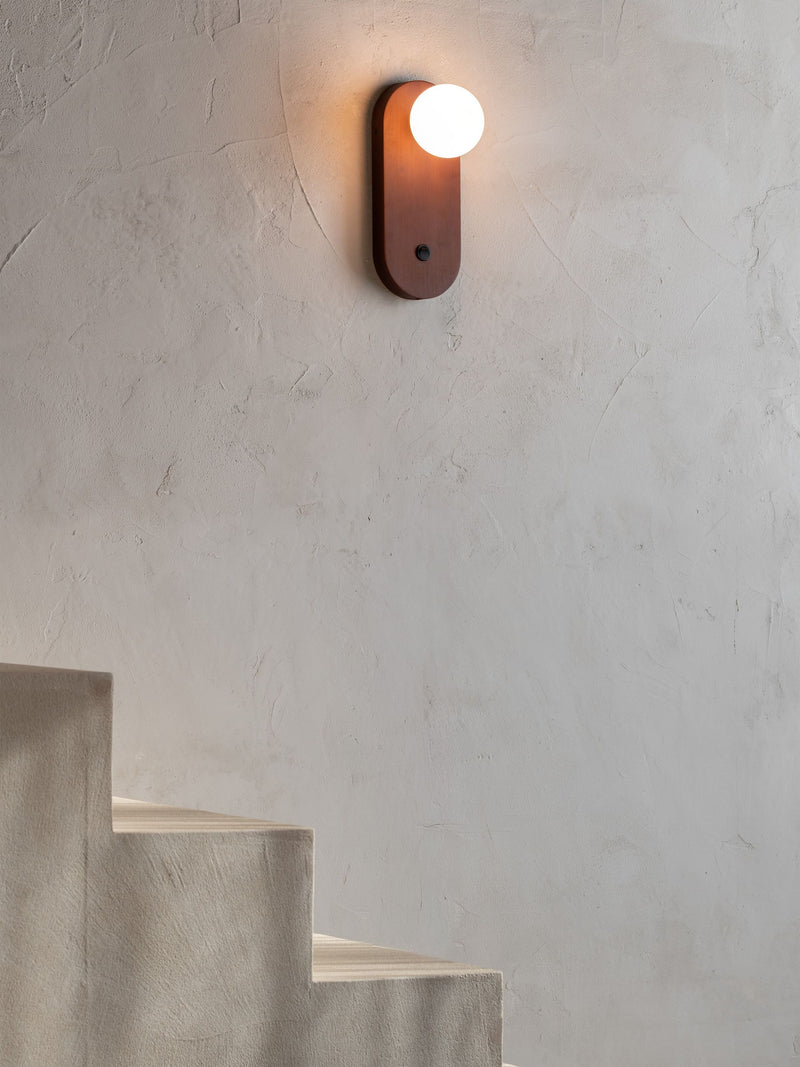 Wandleuchte Java von Good&Mojo mit braunem Bambusgestell und weißem Glasschirm, neben einer Treppe an einer Putzwand.