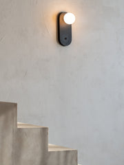 Wandleuchte Java in Schwarz mit weißem Glasschirm, an heller Putzwand über einer Betontreppe montiert.
