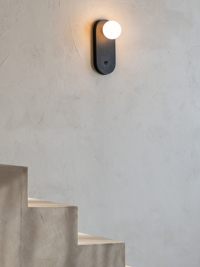 Wandleuchte Java in Schwarz mit weißem Glasschirm, an heller Putzwand über einer Betontreppe montiert.
