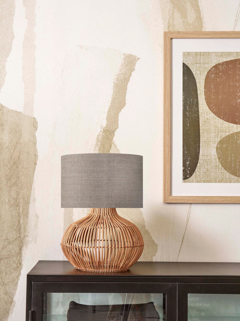 Tischleuchte Kalahari von Good&Mojo mit geflochtenem Rattanfuß und grauem Leinenschirm auf dunklem Sideboard.