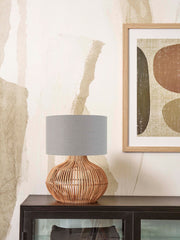 Tischleuchte Kalahari von Good&Mojo mit bauchigem Rattanfuß und grauem Leinenschirm, auf dunklem Sideboard.