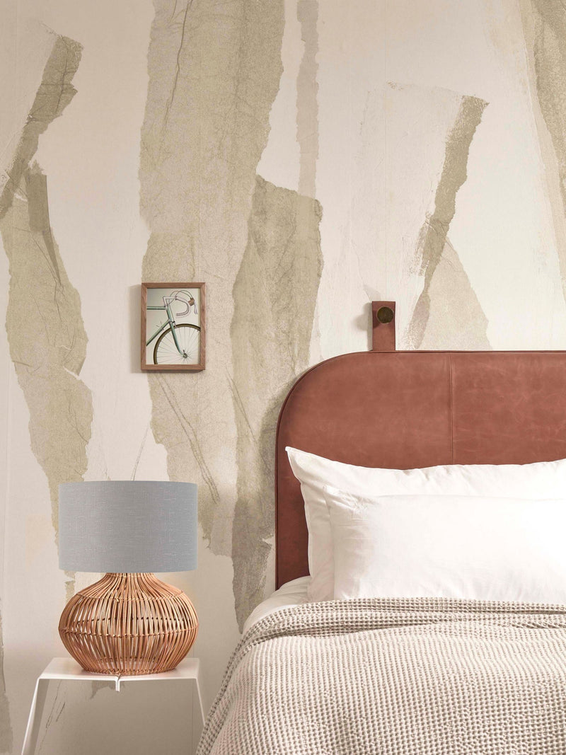 Good&Mojo Tischleuchte Kalahari aus Rattan mit grauem Leinenschirm auf weißem Beistelltisch neben einem Bett.
