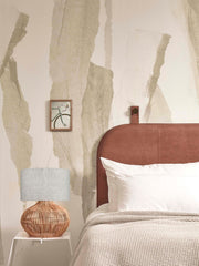 Good&Mojo Tischleuchte Kalahari aus Rattan mit Leinenschirm auf einem weißen Beistelltisch neben einem Bett.