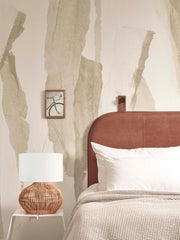 Good&Mojo Tischleuchte Kalahari aus Rattan mit weißem Leinenschirm auf einem weißen Beistelltisch neben einem Bett.