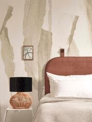 Tischleuchte Kalahari von Good&Mojo mit schwarzem Leinenschirm und Rattanfuß auf einem weißen Beistelltisch neben dem Bett.