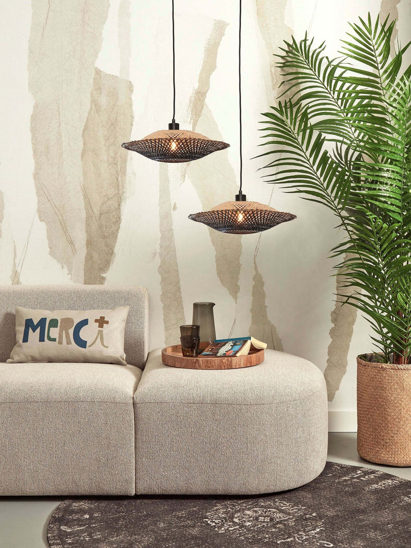 Zwei Hängeleuchten Kalimantan aus Bambus in Schwarz/Natur hängen über einem beigen Sofa vor einer Palme.