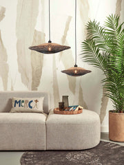 Zwei Hängeleuchten Kalimantan aus Bambus in Schwarz/Natur über einem hellen Sofa mit Palme im Hintergrund.